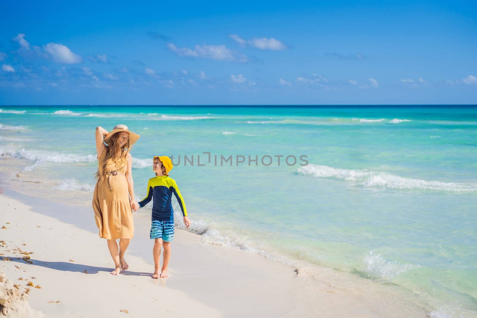 A radiant pregnant mother and her excited son share a tender moment on a serene, snow-white beach, celebrating family love amidst nature's beauty.