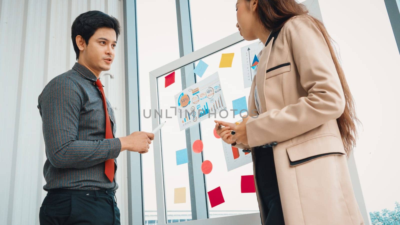 Business people work on project planning board in office and having conversation with coworker friend to analyze project development . They use sticky notes posted on glass to make it organized. Jivy