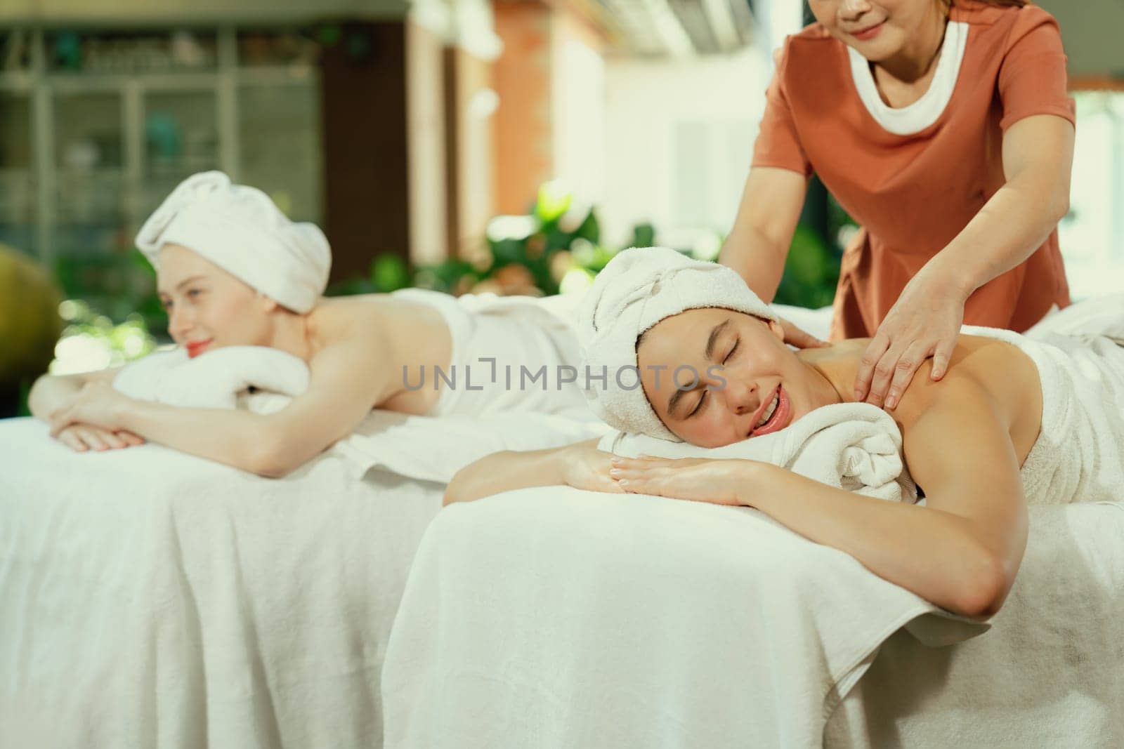 A portrait of two young attractive woman lie on bed during having back massage by a professional masseur at outdoor surrounded by peaceful natural environment. Healthy and beauty concept. Tranquility.