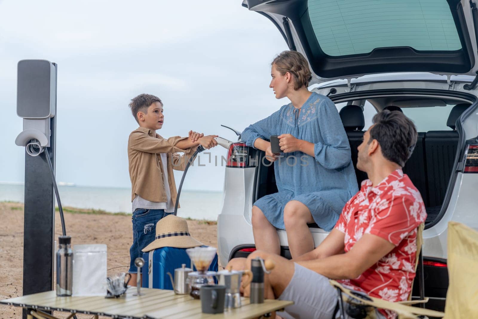 Family vacation trip traveling by the beach with electric car, happy family recharge EV car, enjoying outdoor camping coffee. Seascape travel and eco-friendly car for clean environment. Perpetual