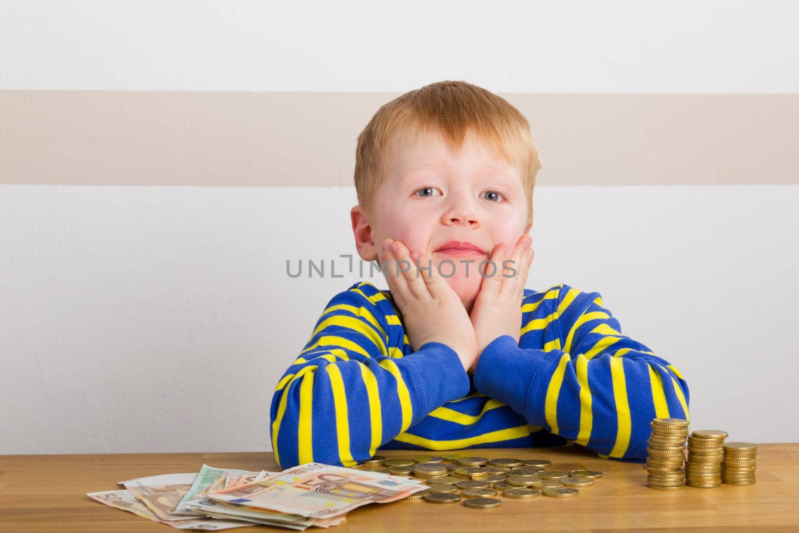 Boy sits in amazement in front of towers of money and bills