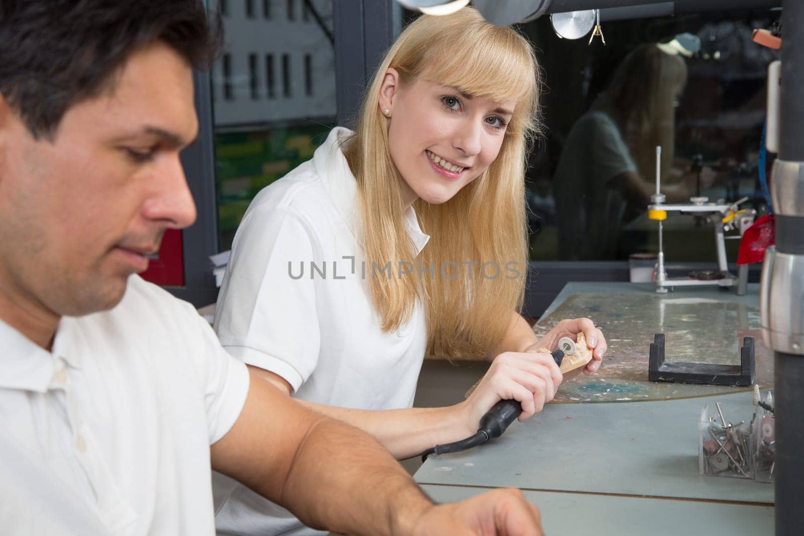 Dental technician smiling into the camera at work. She is producing a dental prosthesis
