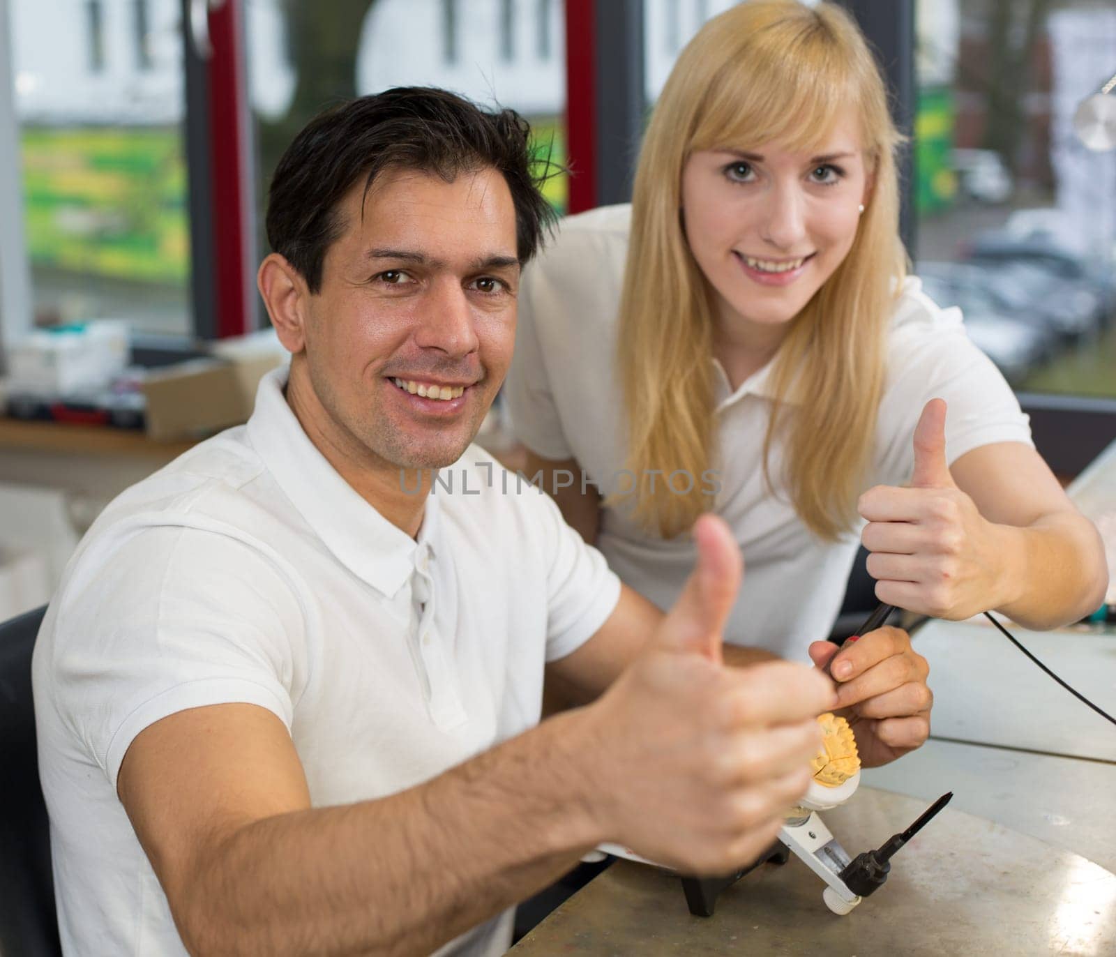 Two dental technicians showing thumbs at work in a lab
