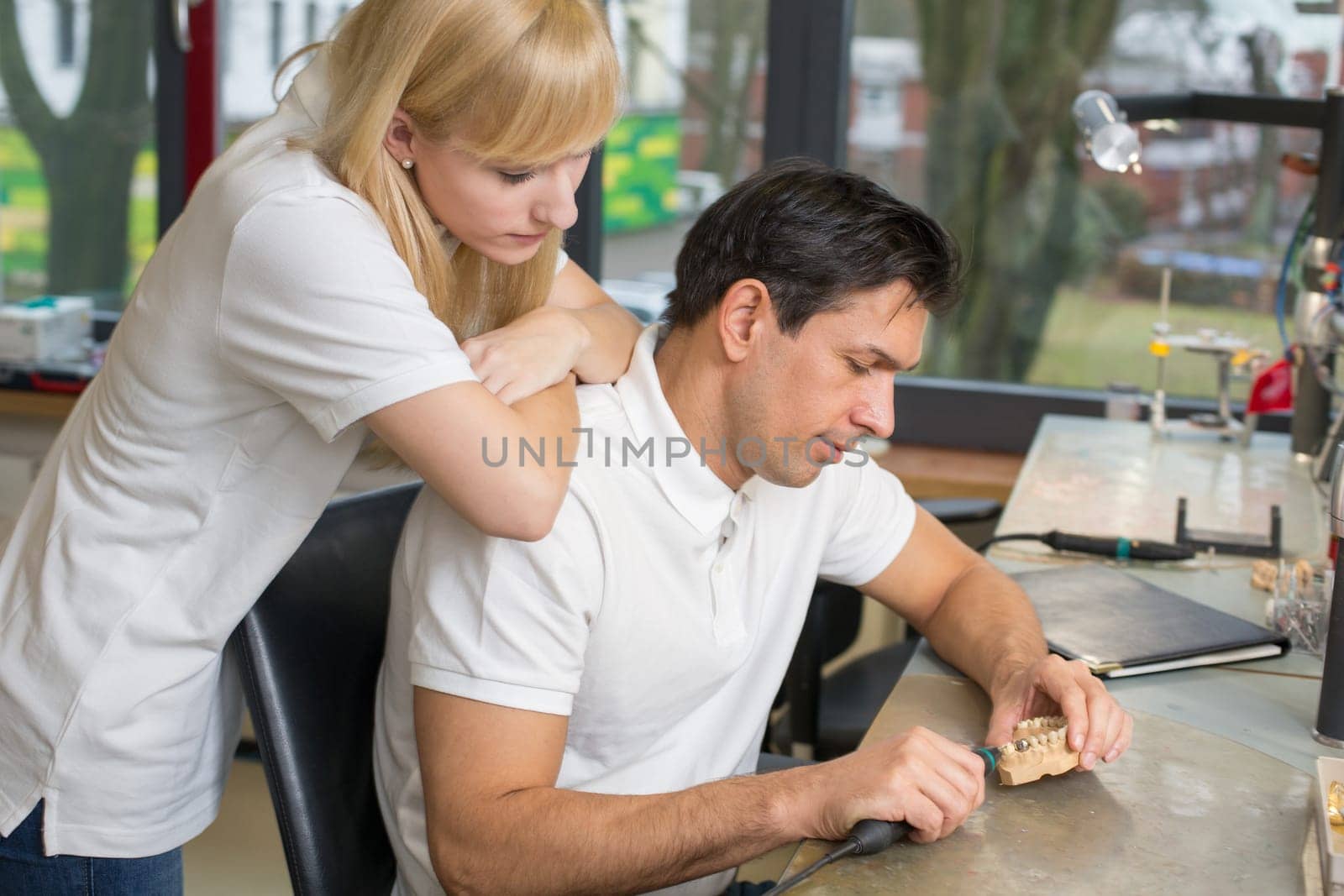 Dental technician watching her friend while working on a prosthesis
