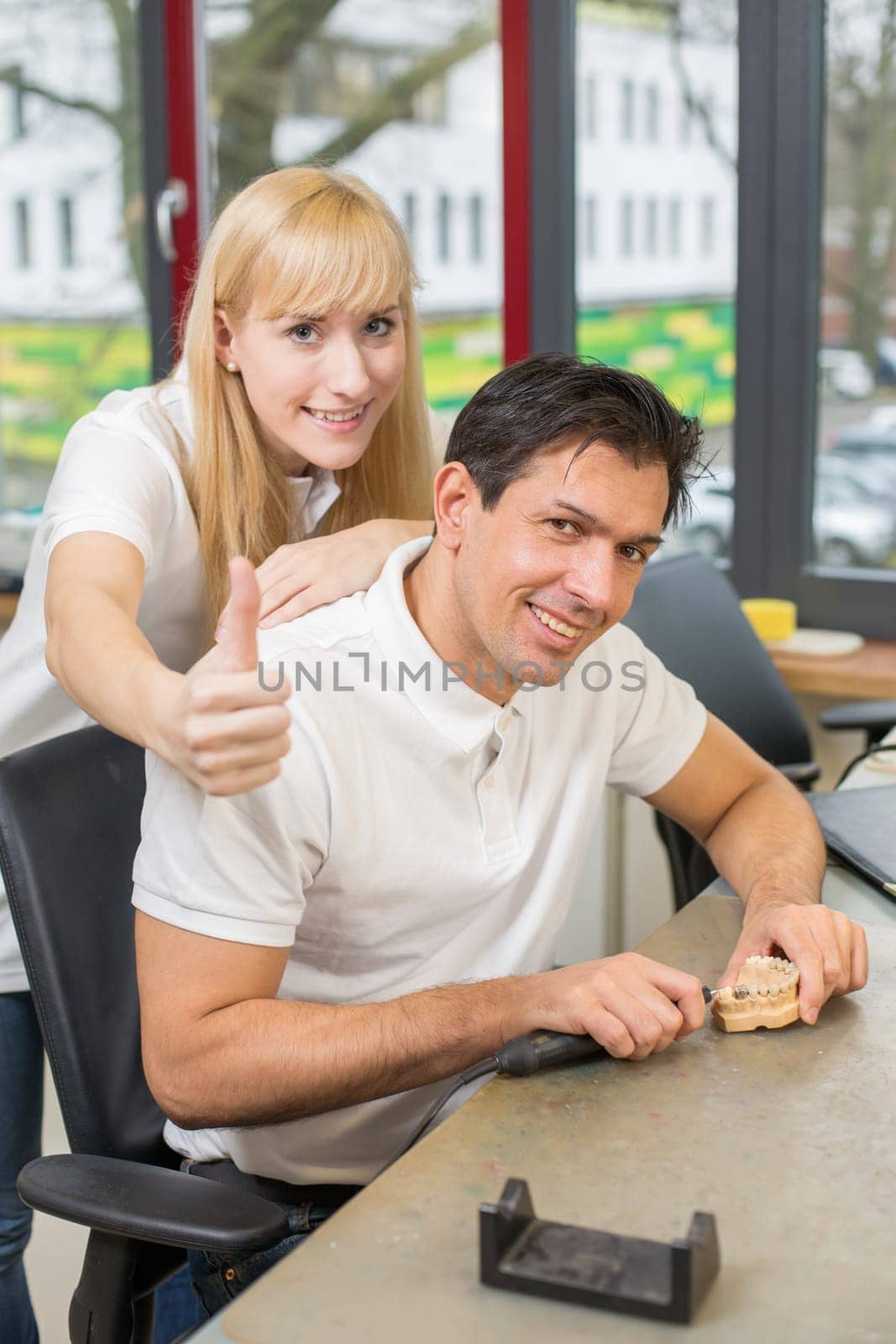 Two friendly technicians at work in dental lab showing thumbs up