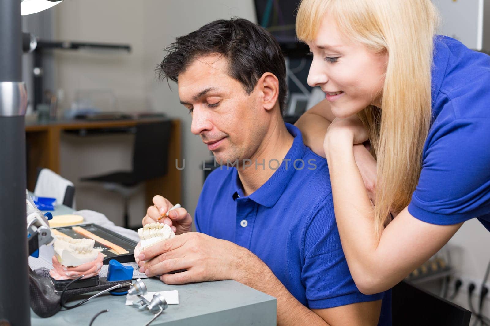 Woman watching dental technician applying porcelain to mold with a brush
