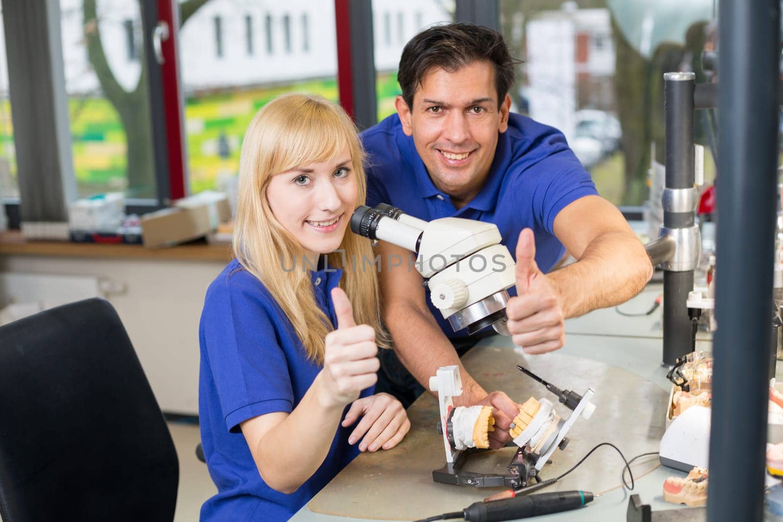 Dental technicians working at a microscope showing thumbs up