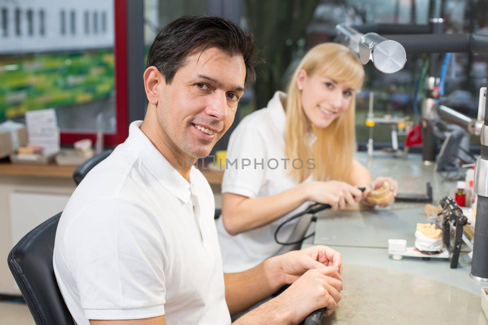 Dental technician in a lab polishing gold tooth and smiling into the camera