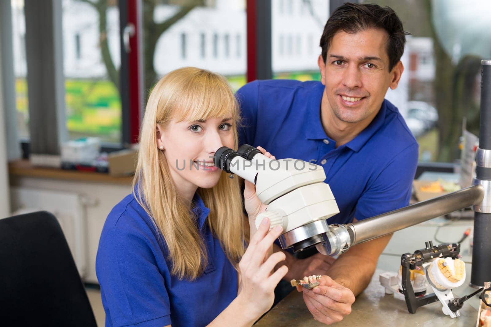 apprentice and dental technician look at prosthesis under a microscope in a lab