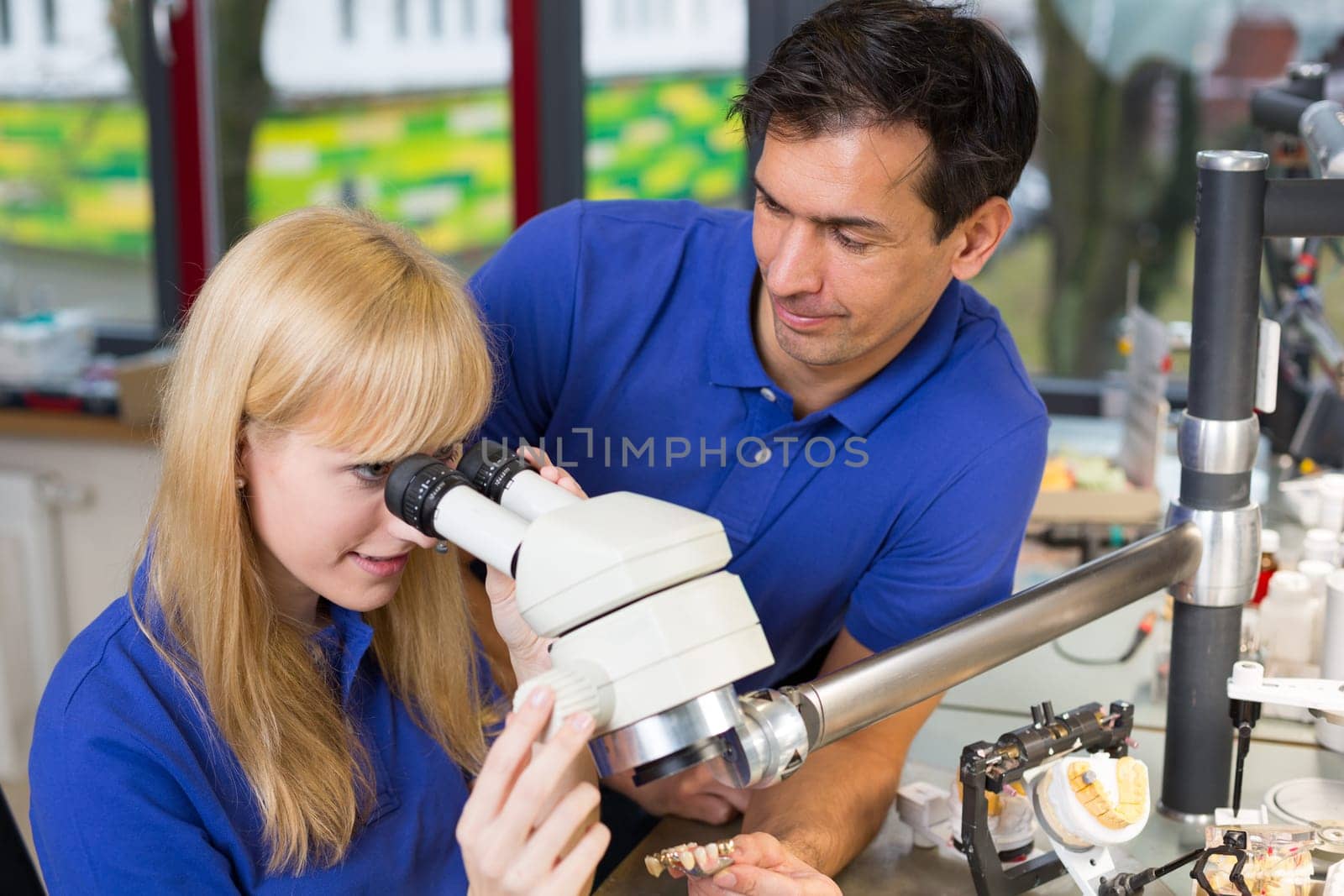 apprentice and dental technician look at prosthesis under a microscope in a lab