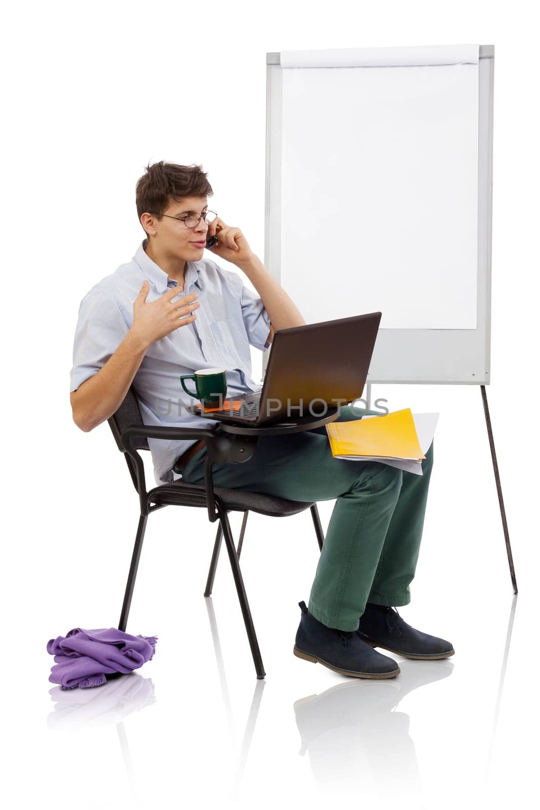 Young man with spectacles speaking on mobile and working on laptop in a workplace