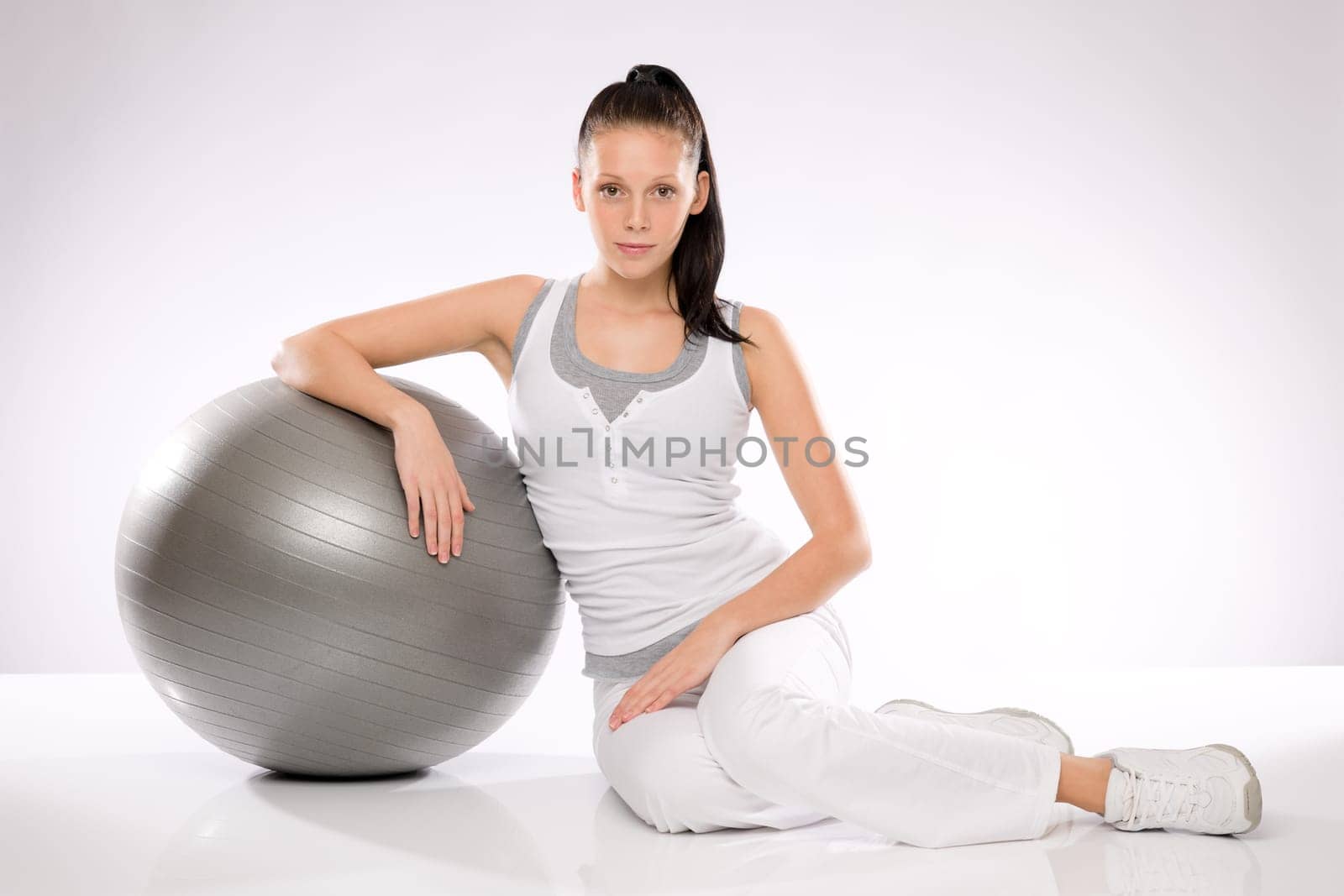 Young Caucasian woman leaning on fitness ball on white background
