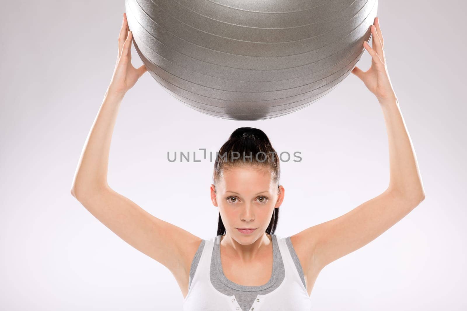 Portrait of young woman exercising with fitness ball held above