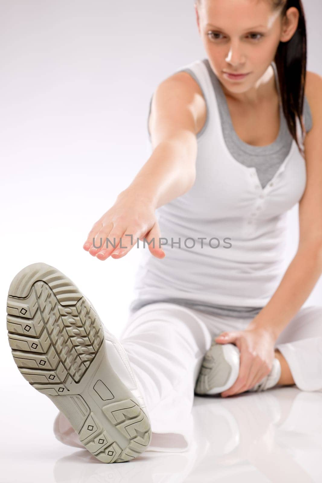 Young Caucasian brunette woman doing stretching exercises on white background