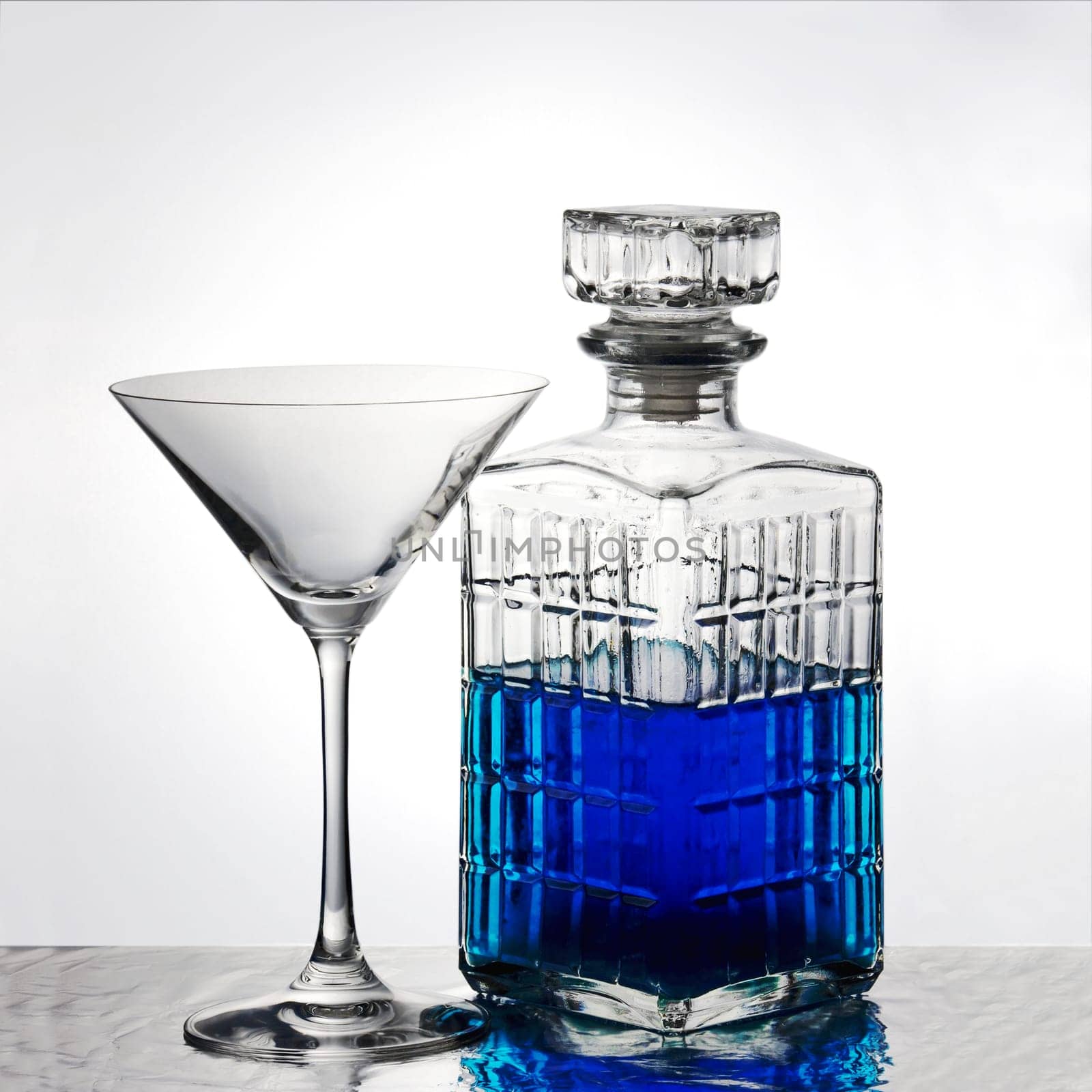A crystal carafe filled with blue liquid and an empty martini glass