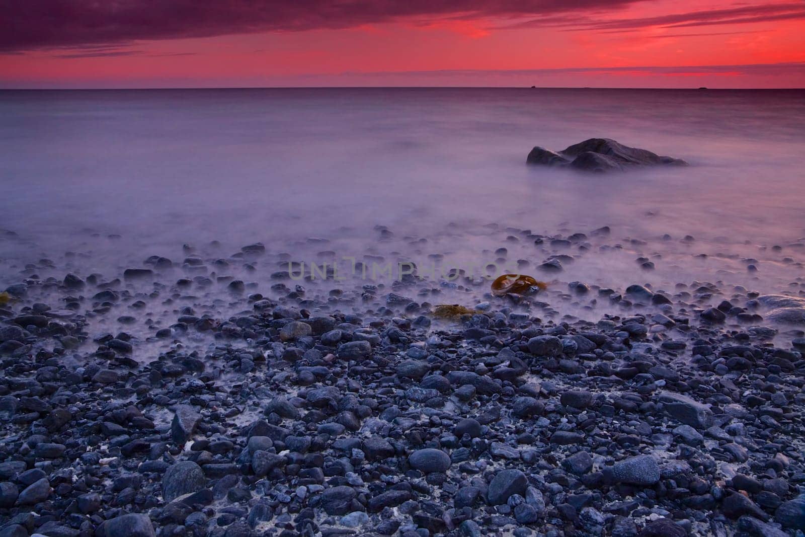 Pebble beach with red skies by sunset on Lofoten islands in Norway