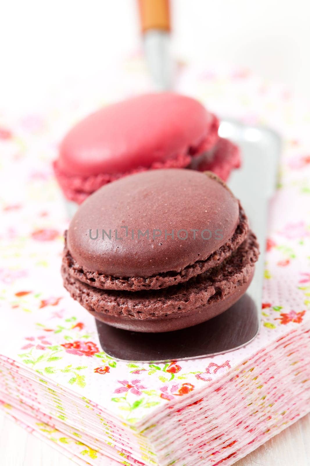 Close-up of two colorful macaroons on serviette and cake server on light background