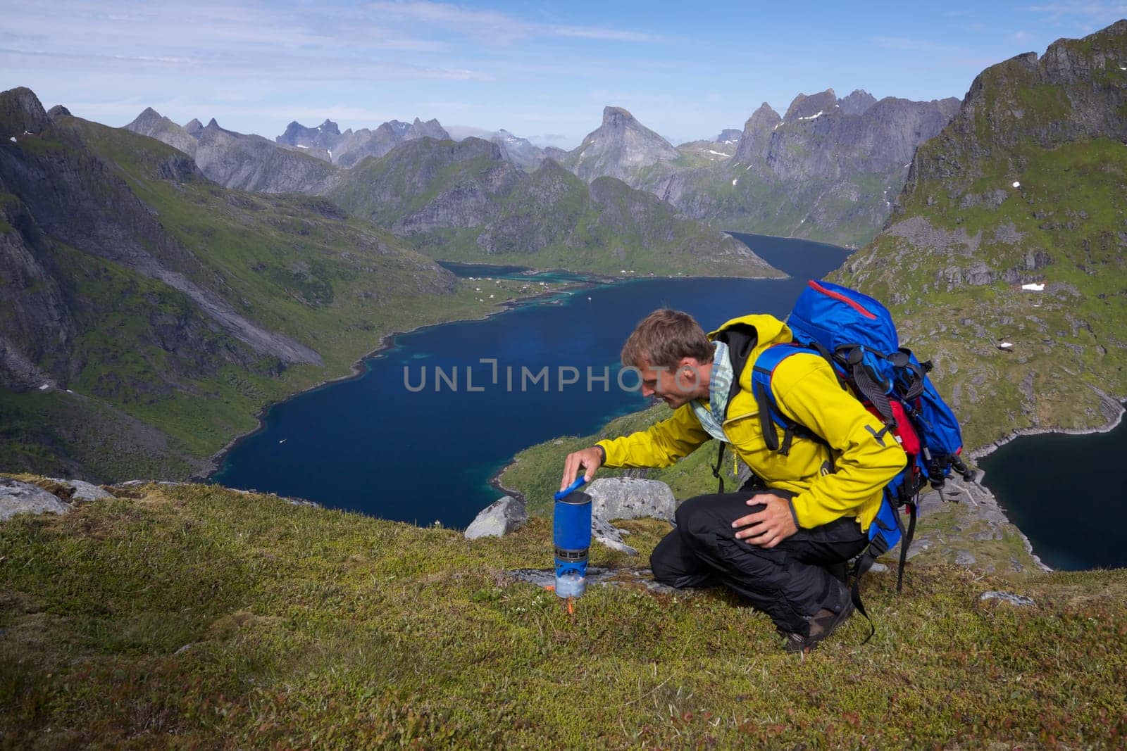 Young active man with backpack hiking on Lofoten islands in Norway on sunny day with scenic panorama in the background