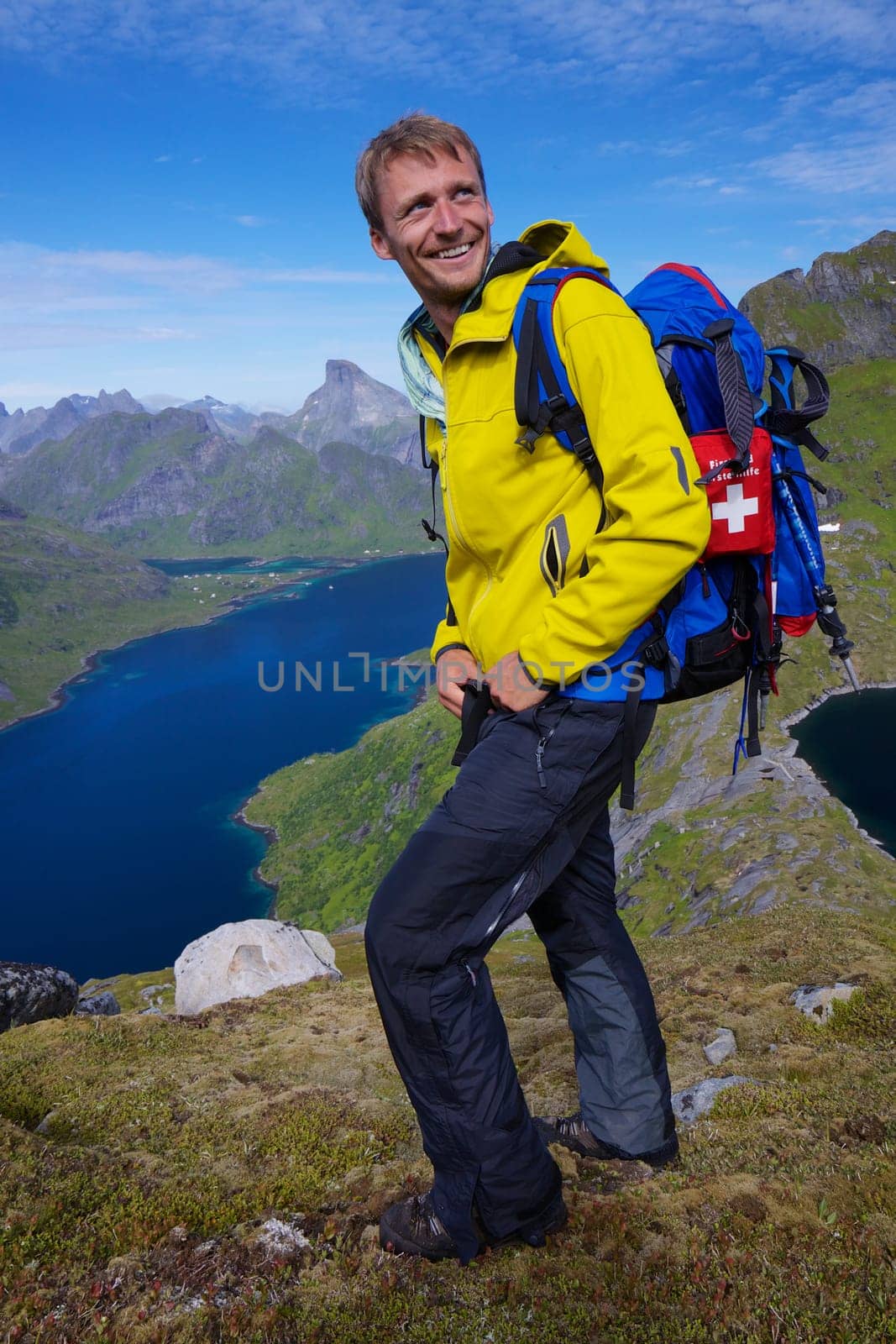 Young smiling active man with backpack hiking on picturesque Lofoten islands in Norway on sunny day
