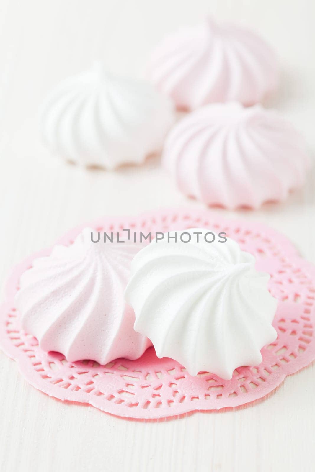 White and pink meringues resting on pink decorative mat on light background