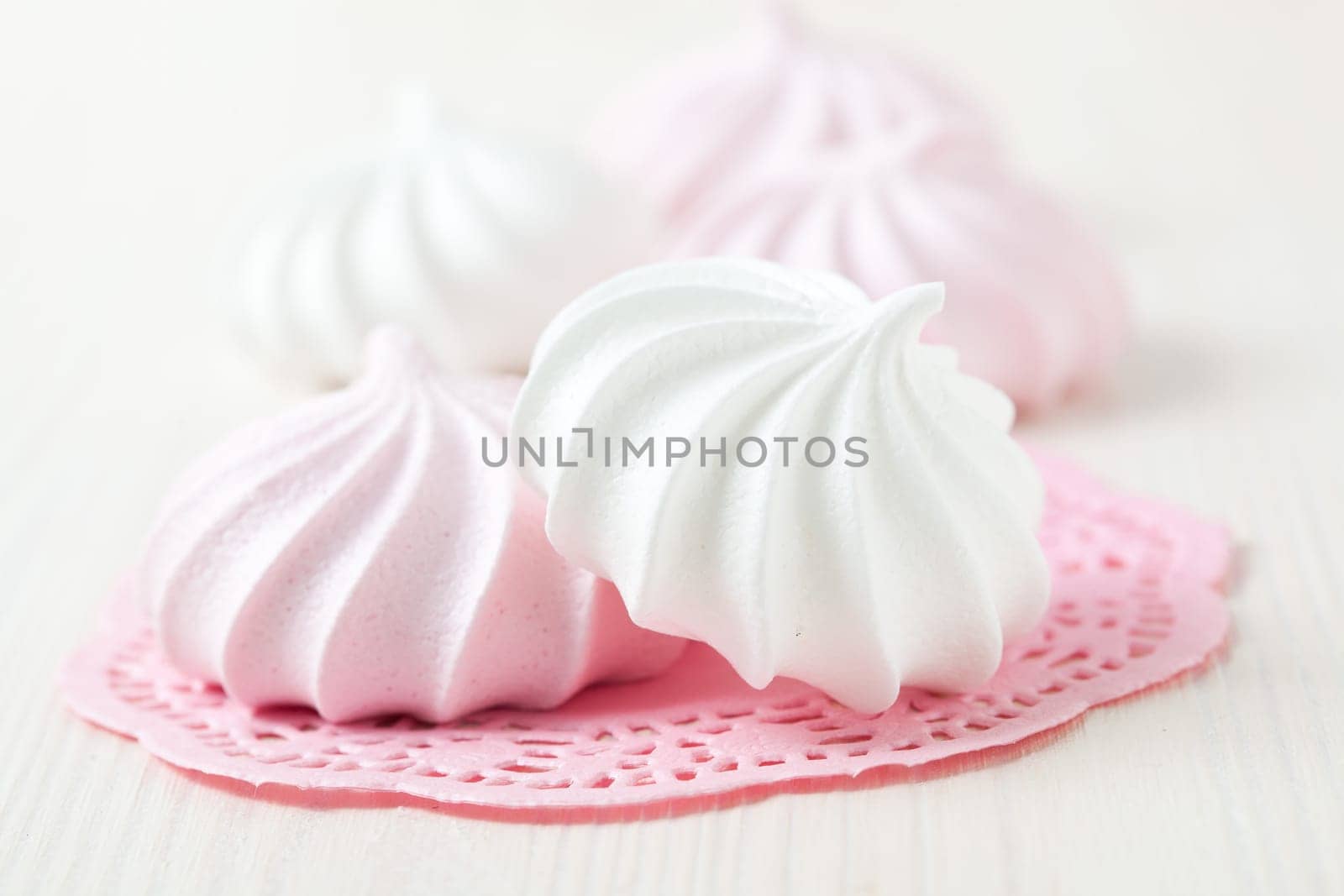 White and pink meringues resting on pink decorative mat on light background
