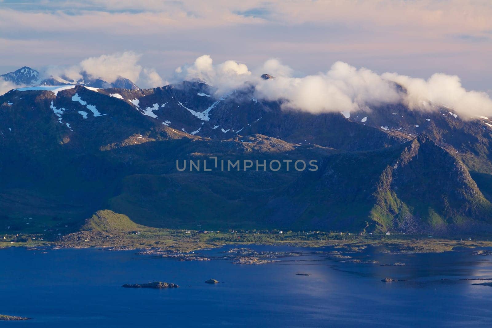 Scenic mountain peaks on Lofoten islands in Norway covered with clouds with small fishing villages on the coast