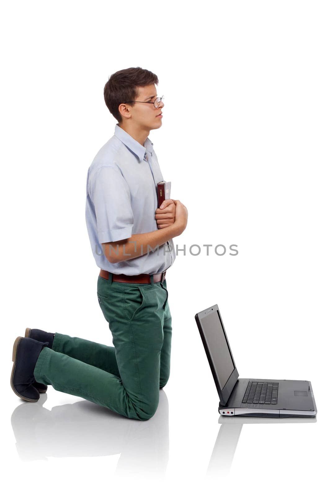 Young man knelt for prayer with the Bible in hand behind a laptop (Concept for  prayer time or for breaking from the worldly things.)