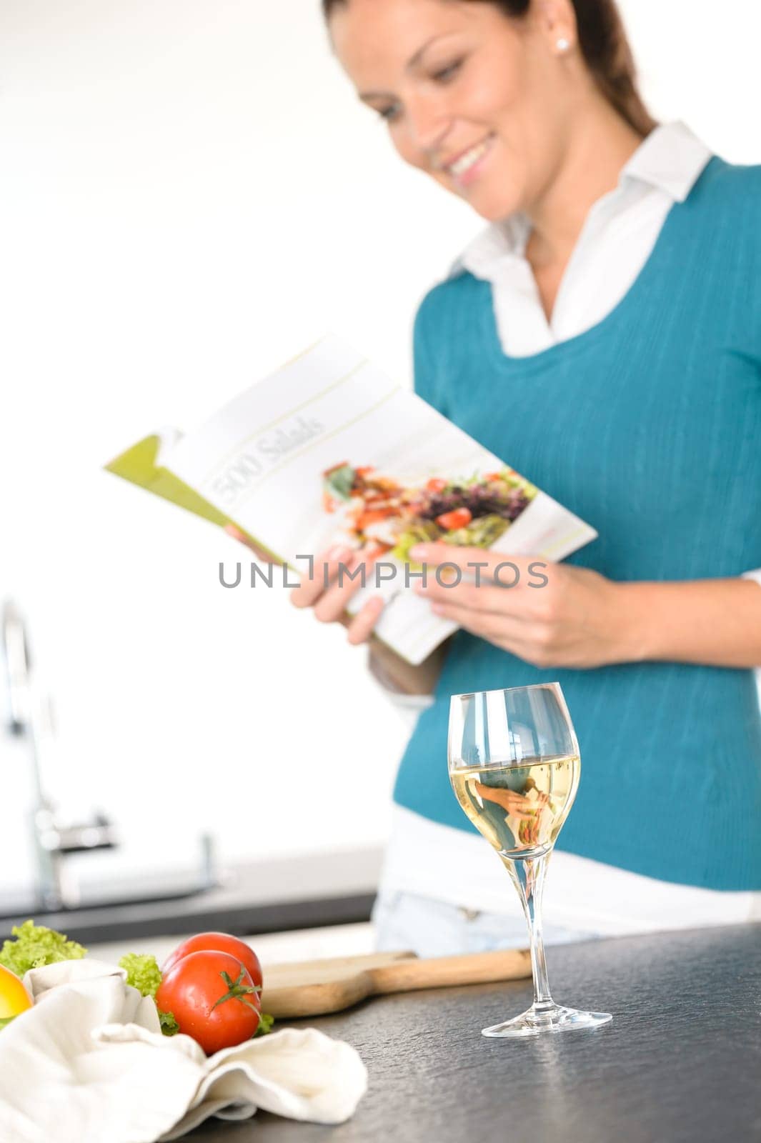 Young woman reading recipe cooking book preparing salad wine kitchen