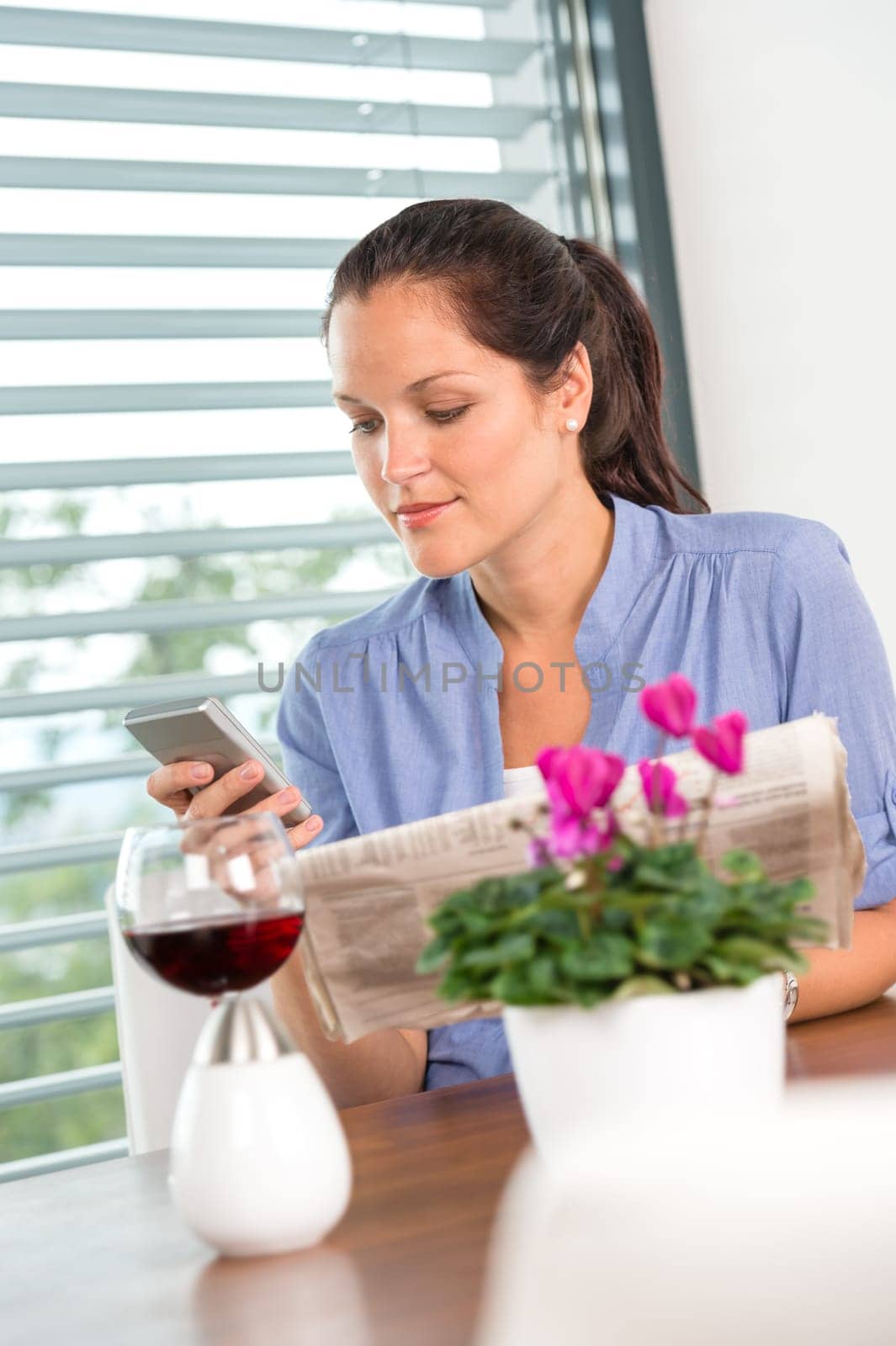 Young woman texting reading newspaper cell phone living room