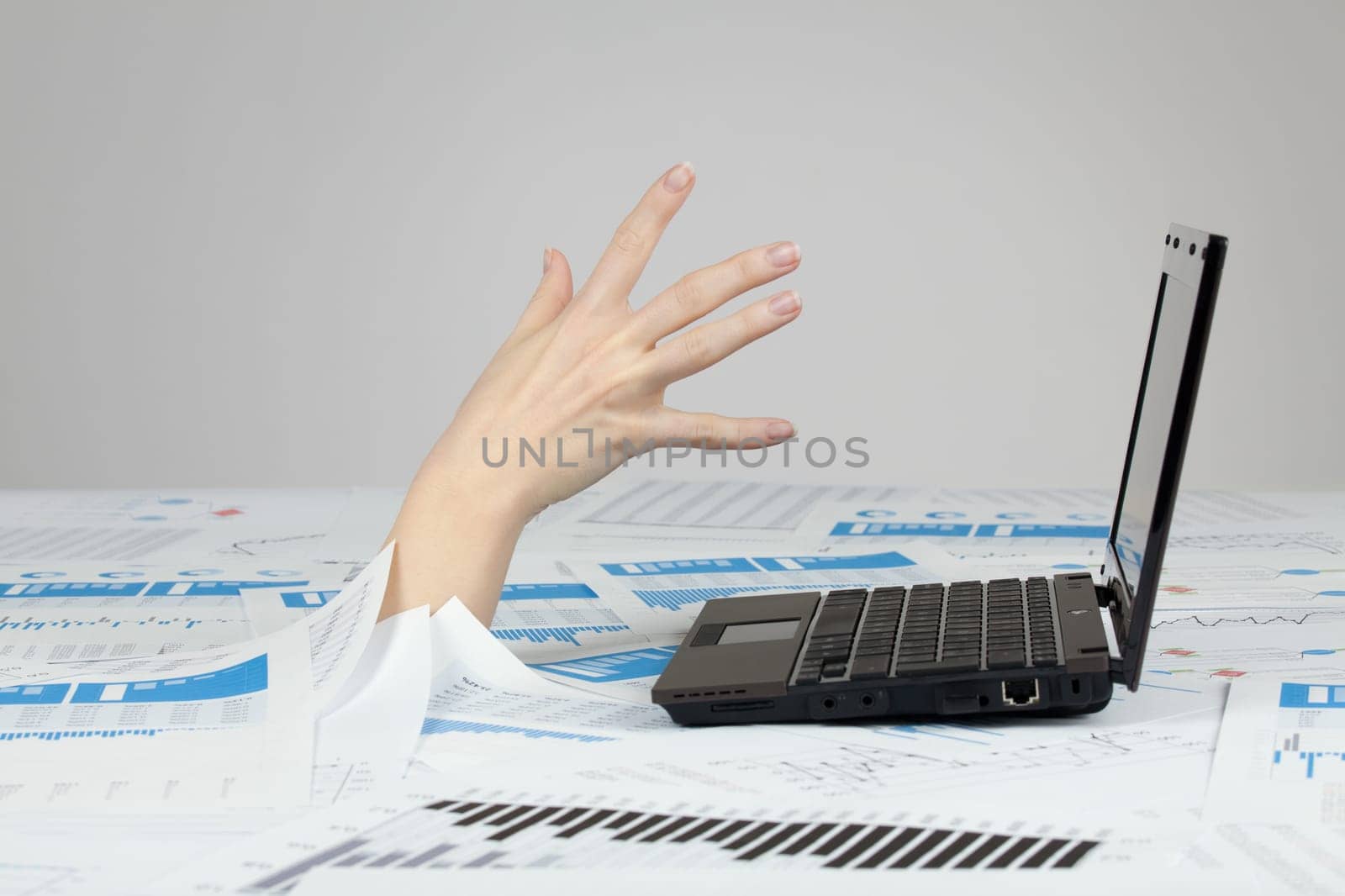 Drowning in paperwork concept. White collar worker reaching out after computer - rescue of paperwork.
