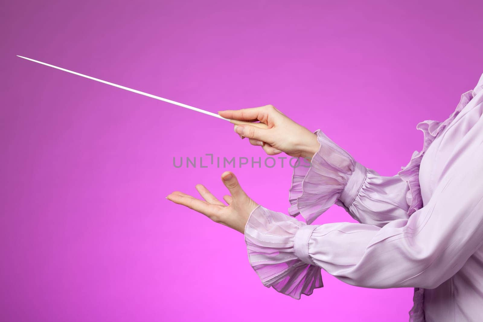 Female orchestra conductor hands, one with baton. Pink background.
