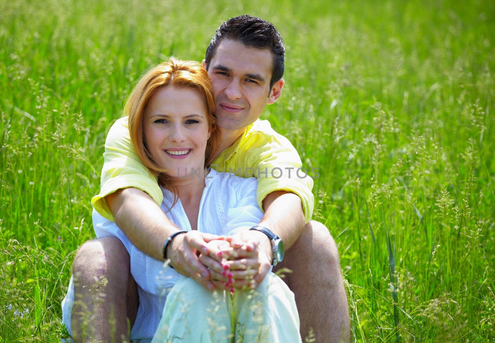 Young couple in their 20s holding eachother outdoor in a grass field.