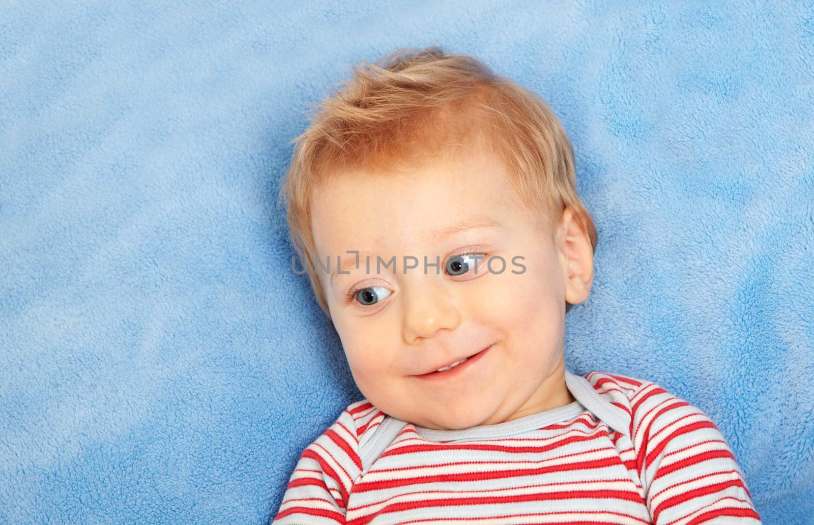 Studio portrait of a happy one year old baby boy smiling and laying down on blue blanket.