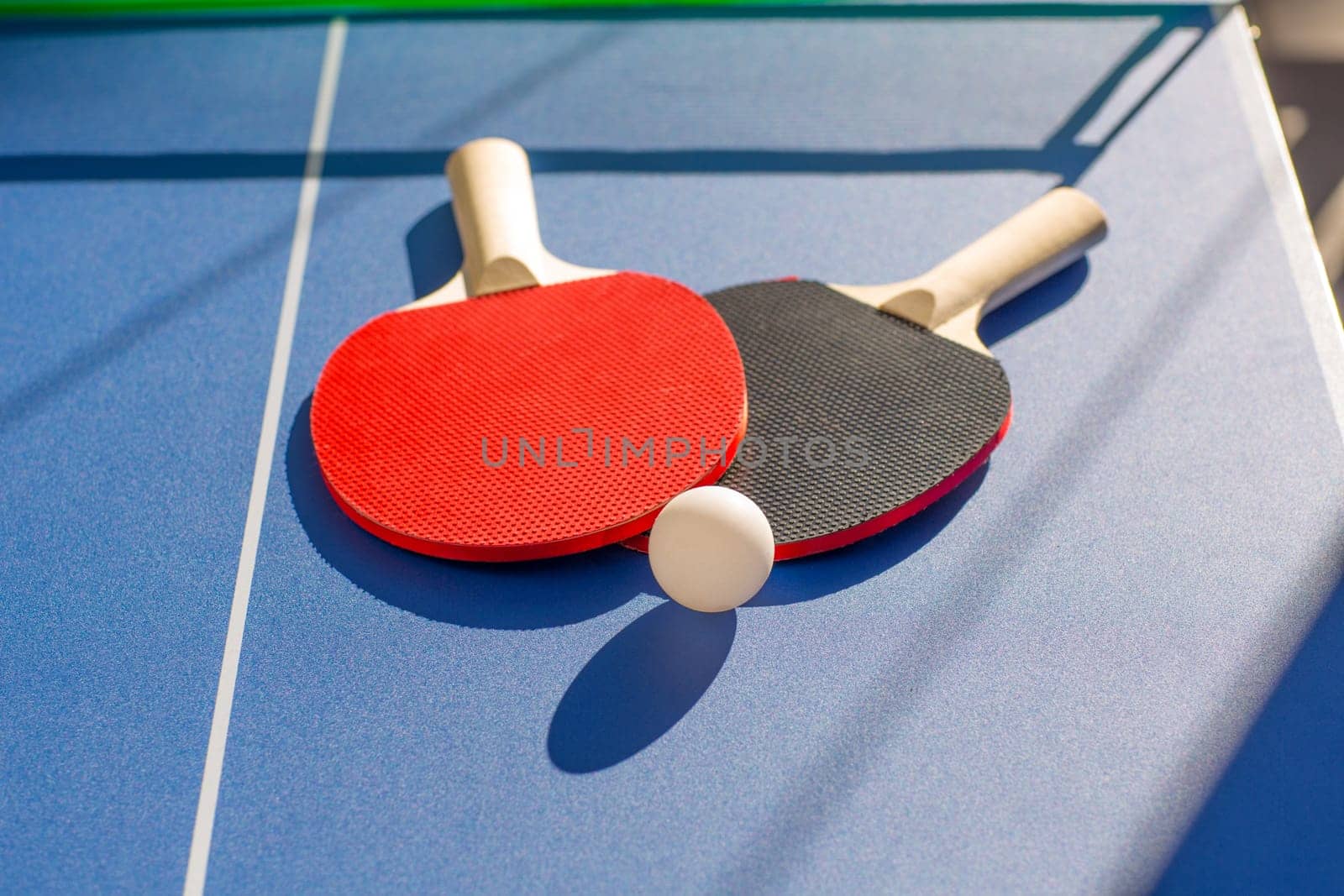 table tennis ping pong two paddles and white ball on blue board