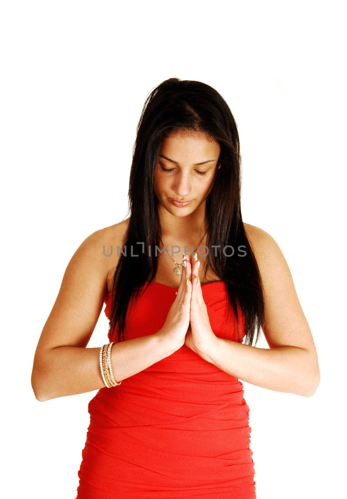 A young pretty teenage girl in a red strapless dress standing for white  background, with folded hands and praying to the Lord.