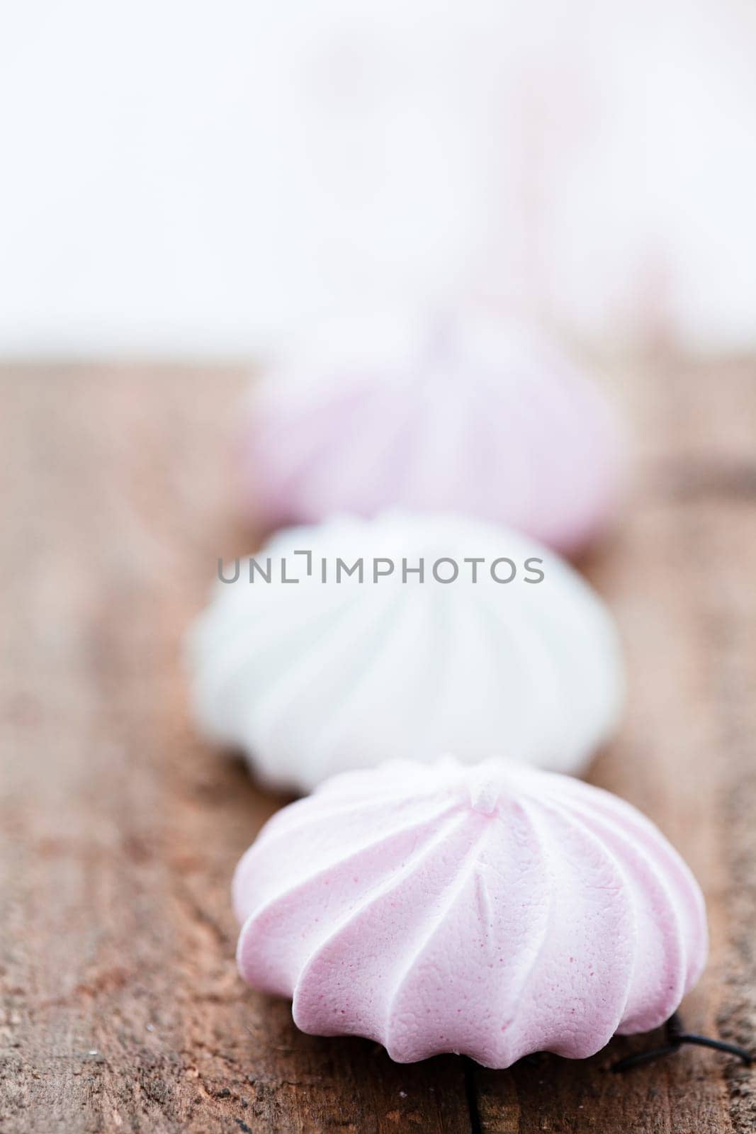 Closeup three pink and white meringues resting on wooden table