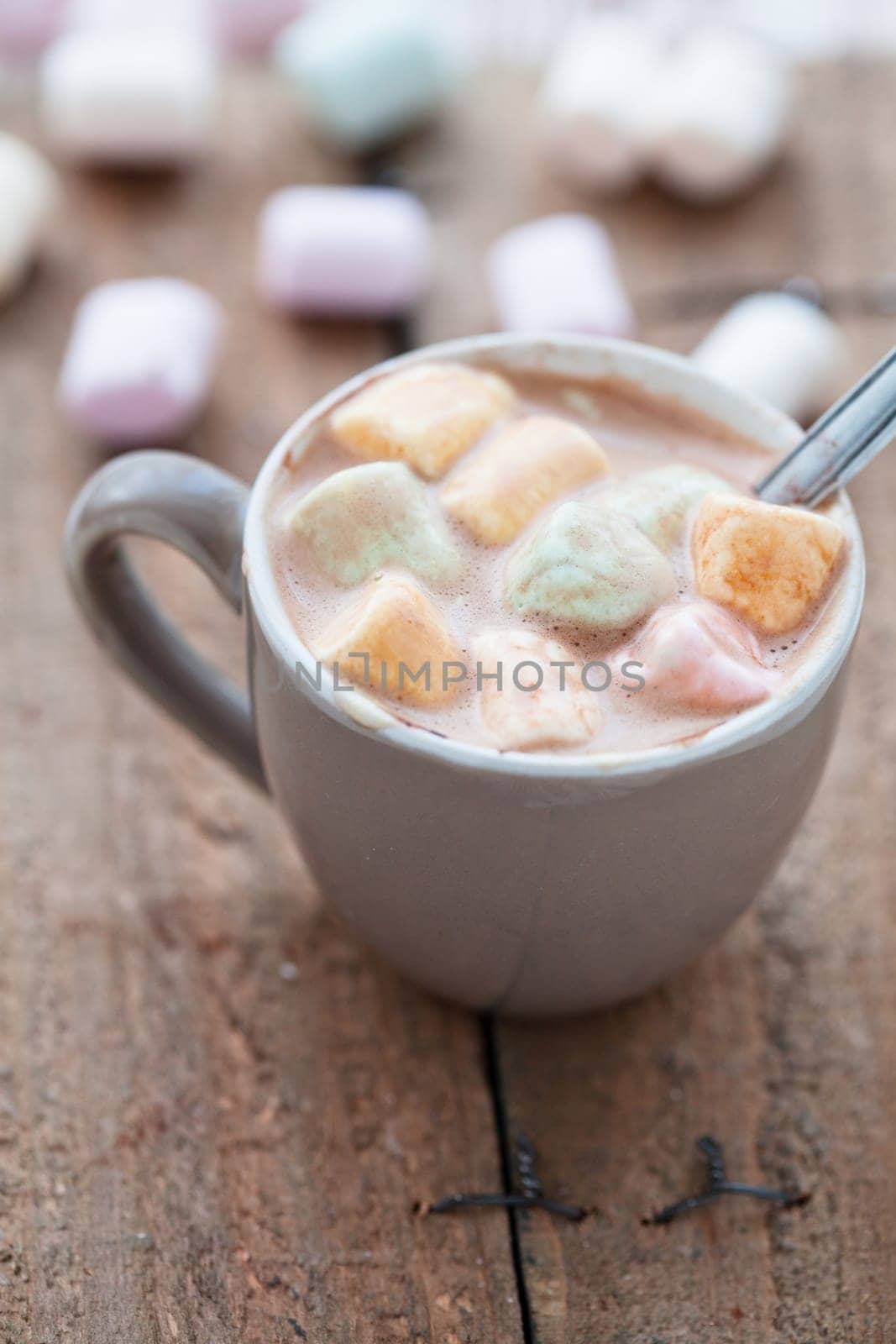 Closeup of cup of hot chocolate with spoon and coloured marshmallows resting on wooden table