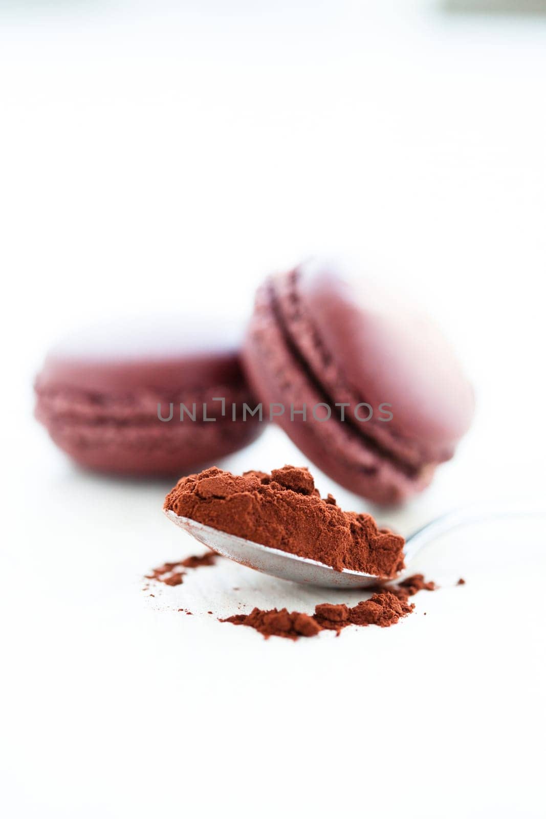 Closeup of cocoa powder in spoon with two macaroons in background
