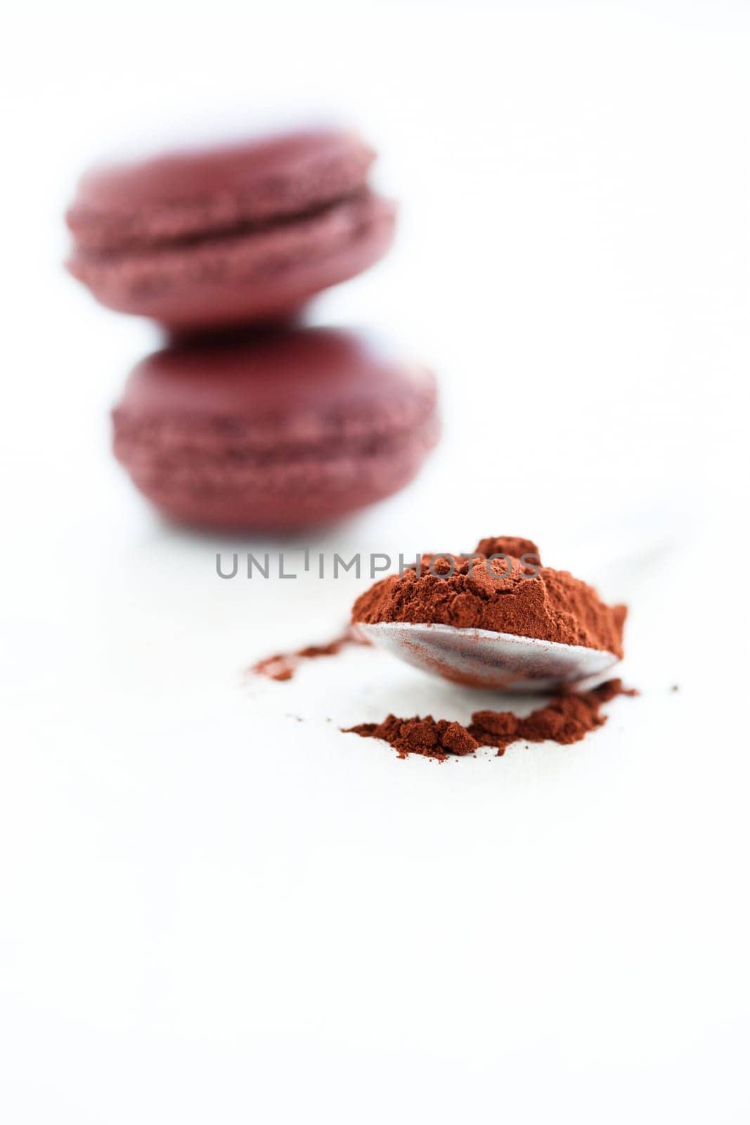 Closeup of cocoa powder in spoon with two macaroons in background