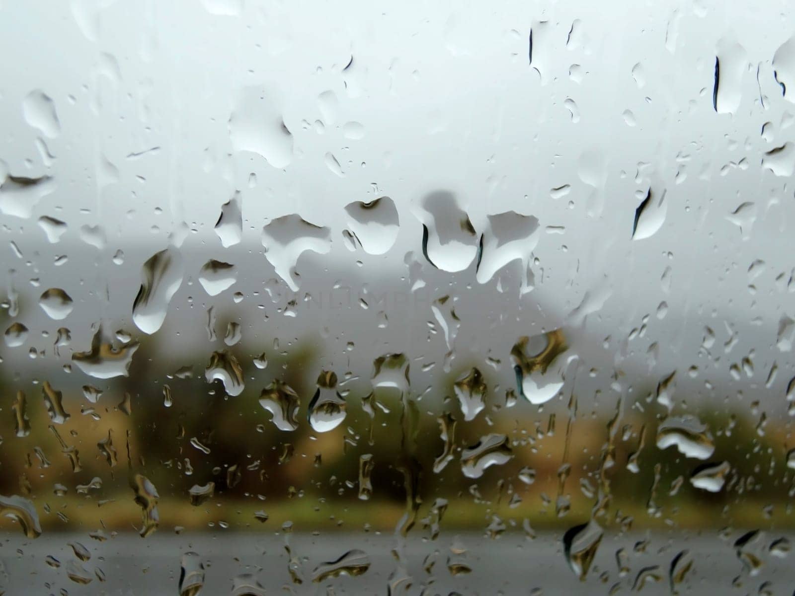 Raindrops on a window on a cloudy day with landscape behind