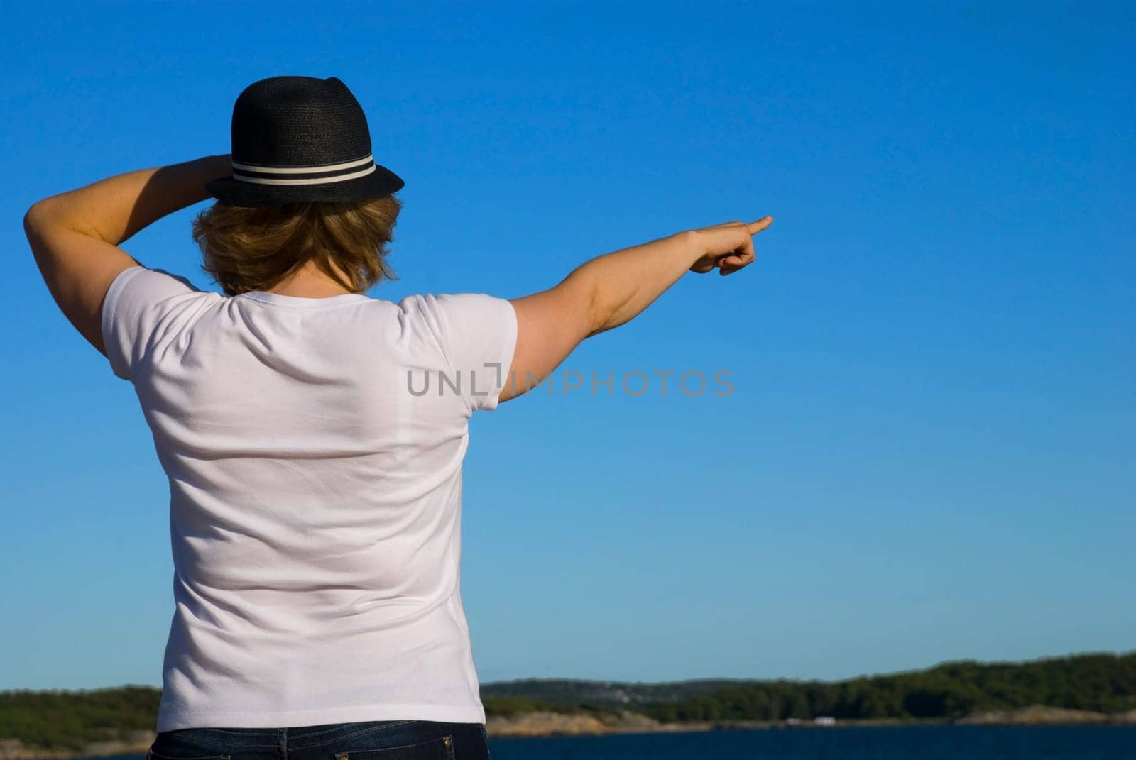 a young woman in white shirt with hat showing the way out to the ocean