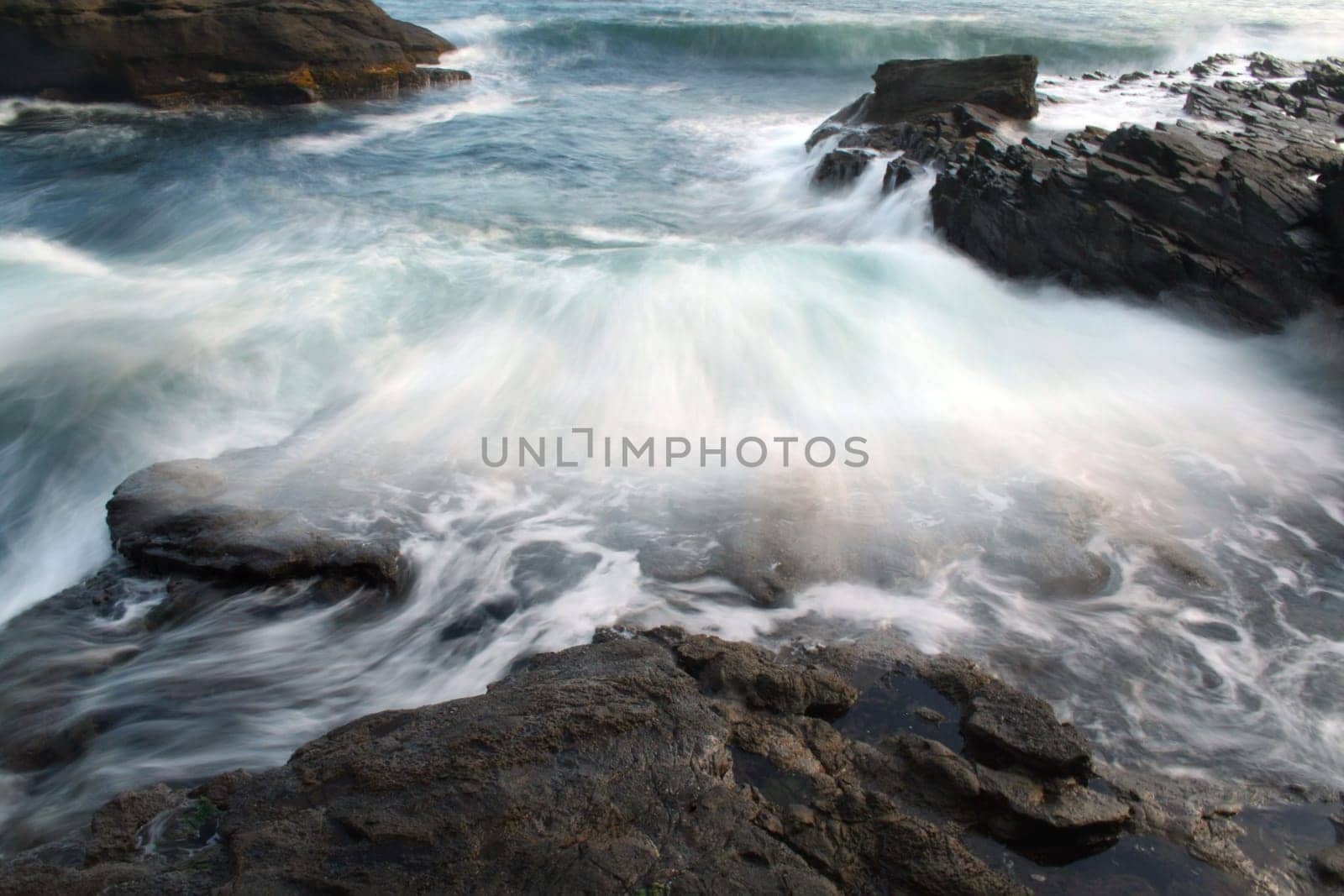 A wave of water crashes over the rocks creating motion. At payzant campground on the Juan de Fuca Trail.