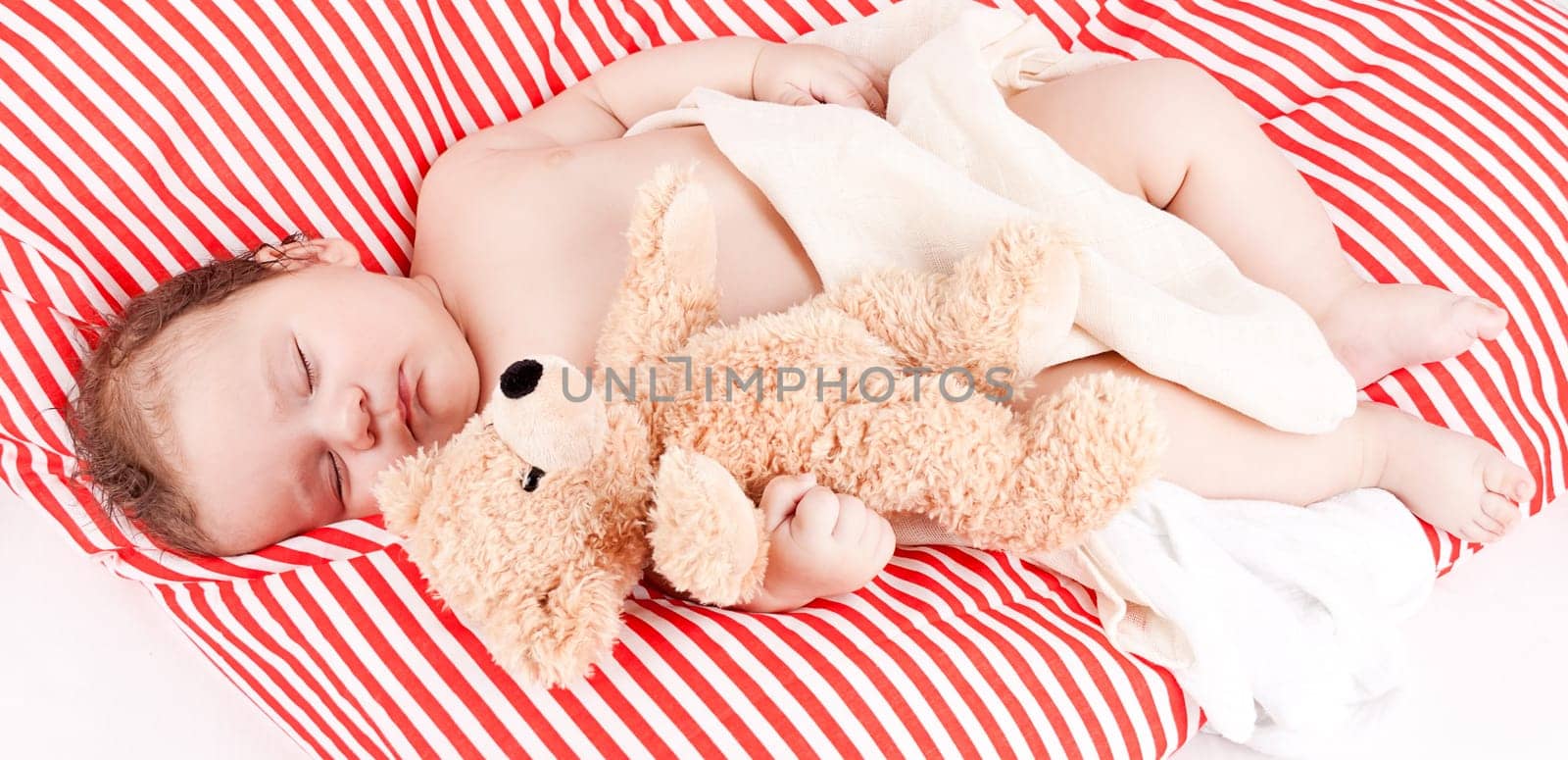 Little cute baby toddler newborn sleeps on a blanket with teddy bear in his arms