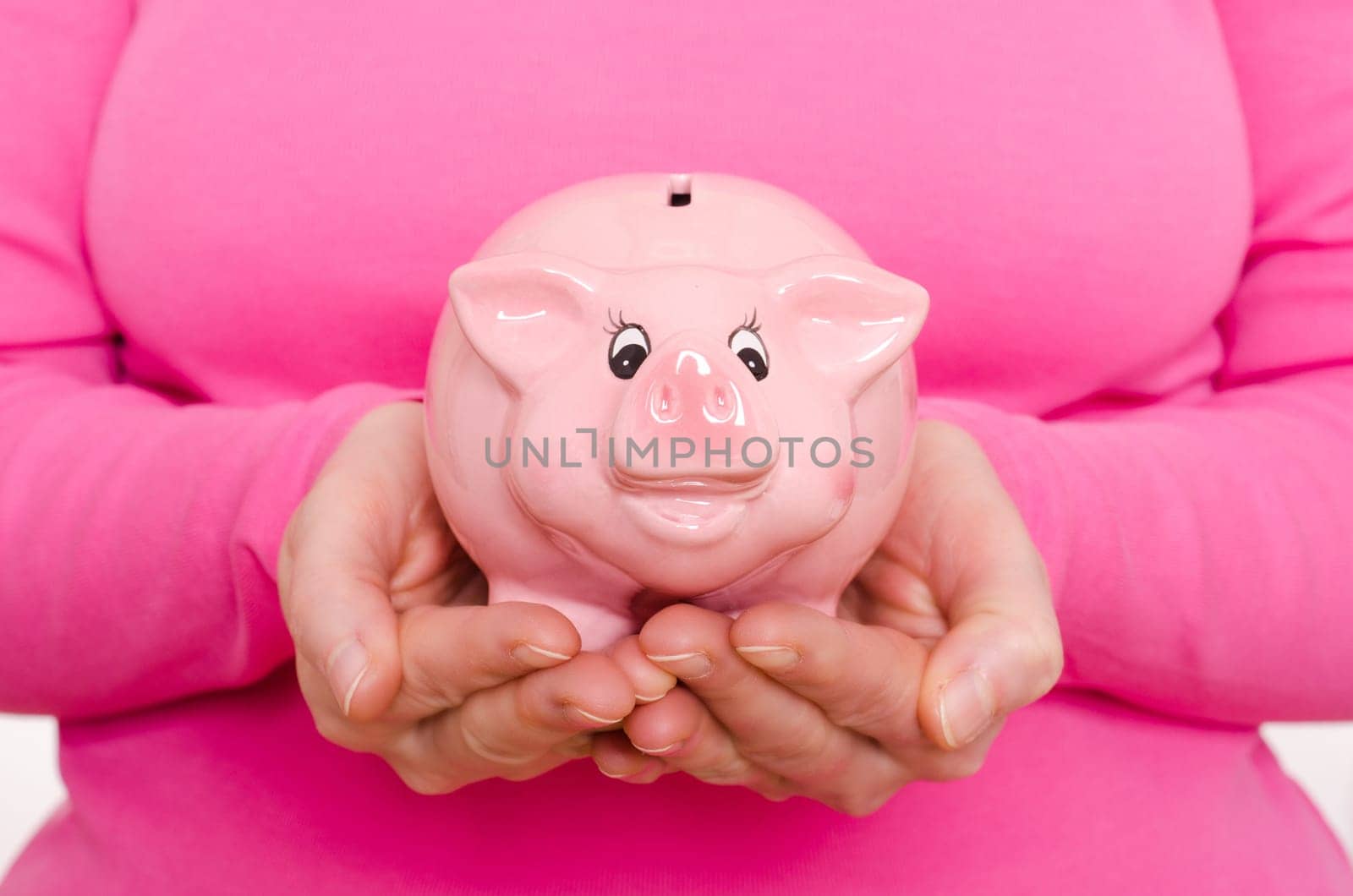 Two female hands holding a pink piggy bank