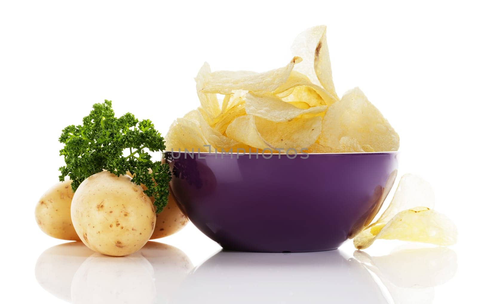 Potato chips in a bowl with potatoes and parsley on white background