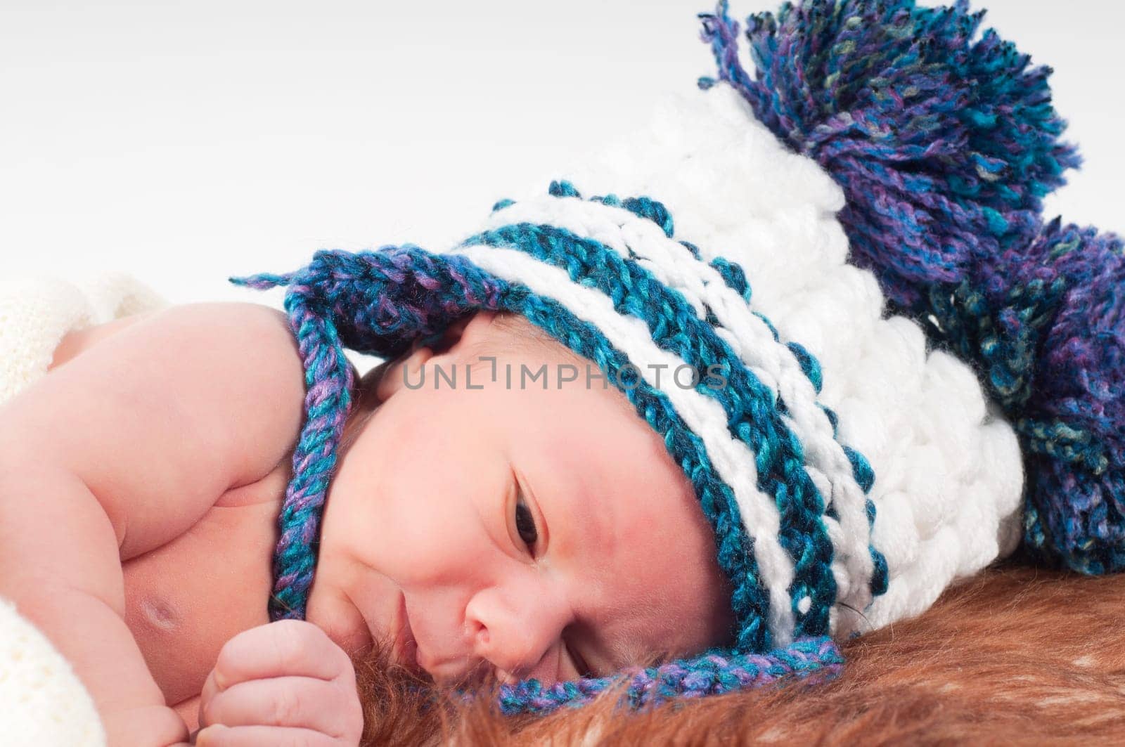 Shot of newborn baby lying on fur in knitted hat with pom-pons
