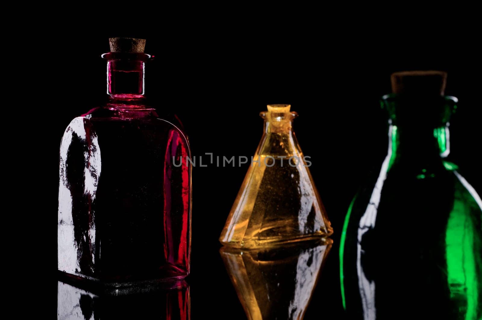 Studio close-up of three different decorative bottles against a black background in sidelight  red square bottle  yellow triangular bottle,green round bottle