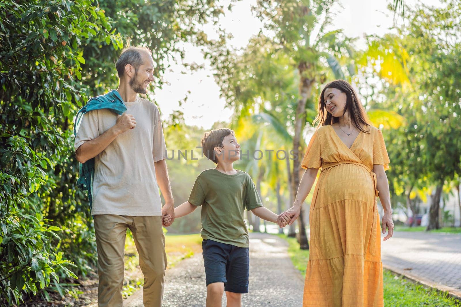 A loving family enjoying a leisurely walk in the park - a radiant pregnant woman after 40, embraced by her husband, and accompanied by their adult teenage son, savoring precious moments together amidst nature's beauty. Pregnancy after 40 concept by galitskaya