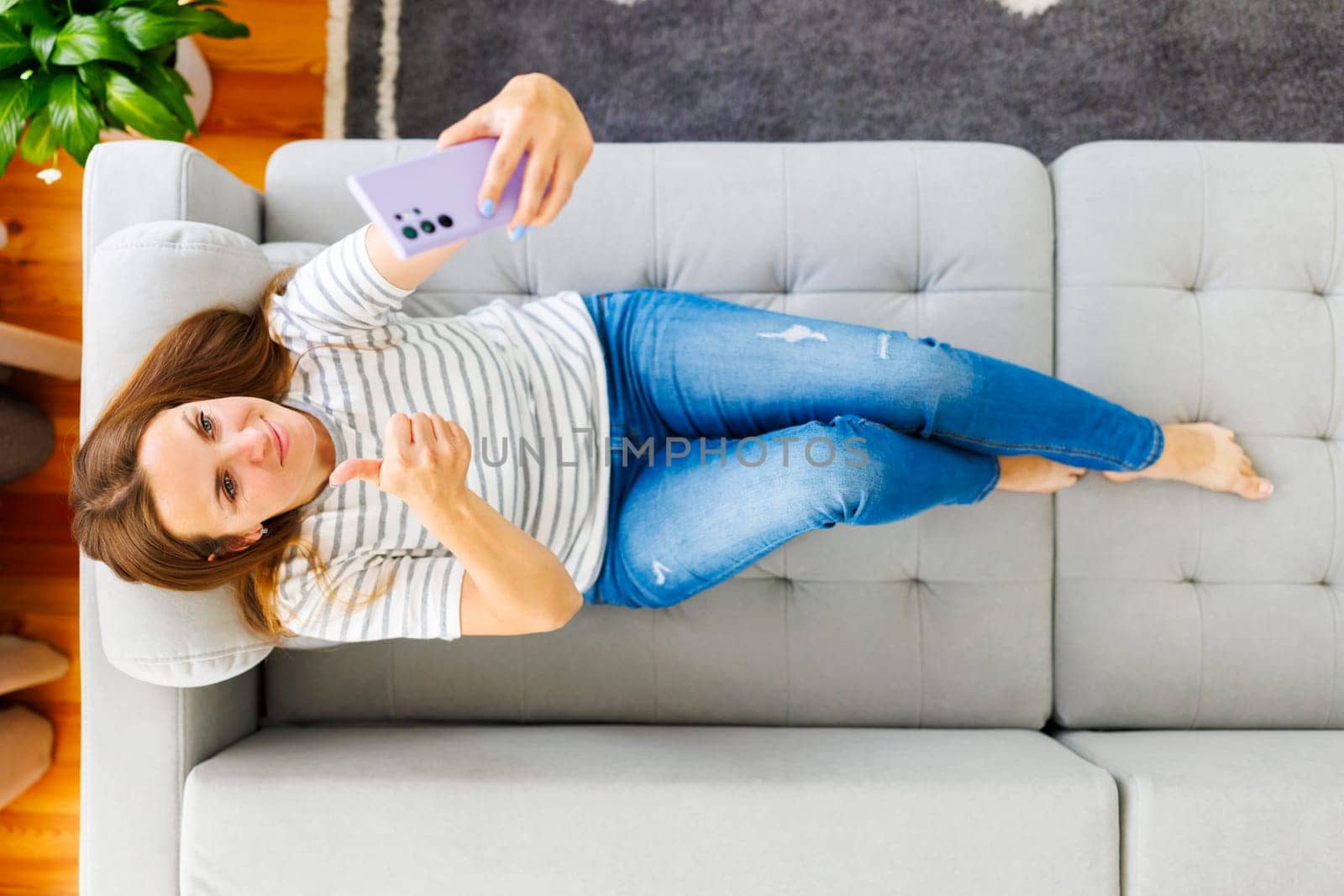 Happy beautiful woman talking on the phone while lying on the sofa at home.
