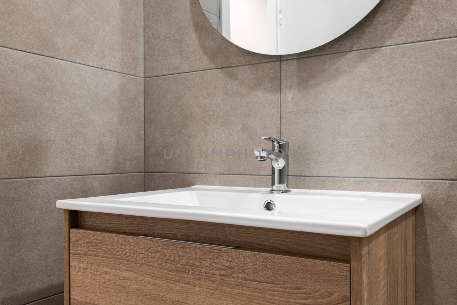 Modern minimalist bathroom interior with stone grey tiles, wooden furniture, white sink and round mirror. Spa bathroom concept by apavlin